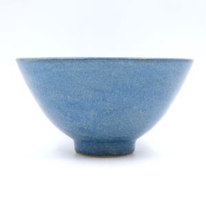 May include: A ceramic bowl with a speckled blue glaze and a smooth, rounded rim. The bowl features a tapered shape that narrows towards a circular base, showcasing a consistent textured finish across the exterior surface in a vibrant blue hue.
