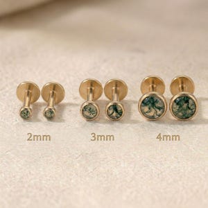 Puede incluir: Un conjunto de pendientes de botón dorados con piedras de ágata musgosa verde. Los pendientes se muestran en pares, con tamaños de 2 mm, 3 mm y 4 mm. Los pendientes tienen una parte posterior plana y una piedra redonda engastada.