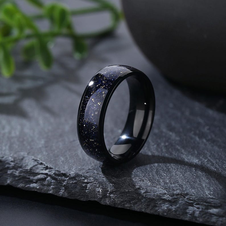 Puede incluir: Un anillo negro con un acabado moteado azul oscuro. El anillo est&aacute; hecho de carburo de tungsteno y tiene un acabado pulido.