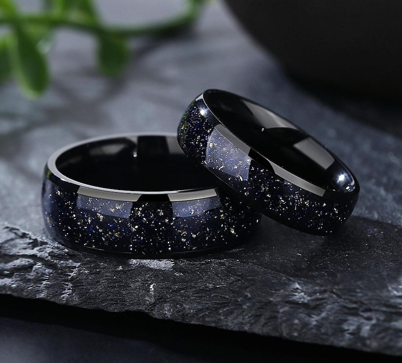 Puede incluir: Dos anillos negros con un patr&oacute;n moteado azul y dorado. Los anillos est&aacute;n apilados uno encima del otro.