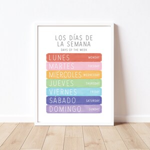 May include: A colourful printable wall art poster with the days of the week in Spanish and English. The poster features a rainbow colour scheme with each day of the week written in a different colour.