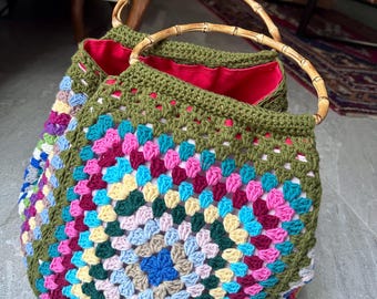 May include: A green crocheted tote bag with a colorful granny square pattern and bamboo handles.