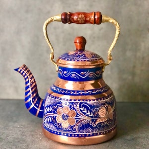 May include: A blue and copper teapot with a gold handle and floral designs. The teapot has a round body and a lid with a knob.