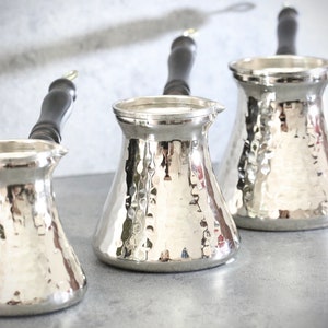 Peut inclure: Trois cafetières turques en argent avec des finitions en métal martelé et des poignées en bois noir.