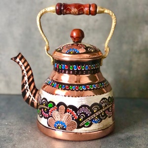 May include: A copper teapot with a painted floral design in black, red, green, blue, and white. The teapot has a wooden handle and a gold-colored spout.