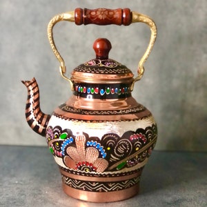May include: A copper teapot with a gold handle and a painted floral design in black, white, red, blue, and green.
