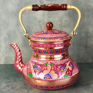 May include: A traditional Turkish tea kettle with a pink and copper body. The kettle is decorated with intricate floral patterns in shades of pink, green, blue, and gold. The kettle has a brass handle and spout.