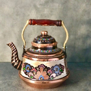 May include: A copper teapot with a decorative floral design. The teapot features a dark brown handle with a wooden grip, a copper lid, and a spout with a striped pattern. The body of the teapot is adorned with colorful floral patterns.