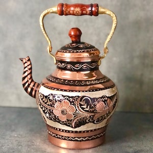 May include: A copper teapot with a wooden handle and intricate floral designs. The teapot has a black and copper finish and a gold-colored spout.