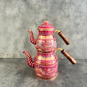 Può includere: Un set da tè turco tradizionale a due livelli. La teiera è rosa con intricati disegni dipinti a mano in oro, rosso, blu e verde. La teiera ha due manici in legno.
