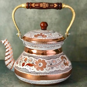 May include: A white and copper teapot with a floral design. The teapot has a wooden handle and a gold-colored spout.