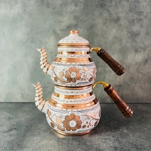 Può includere: Teiera turca in rame e bianca con disegni floreali. La teiera ha un design a due livelli con coperchio e due manici in legno. Gli accenti in rame e i motivi floreali creano un look elegante.