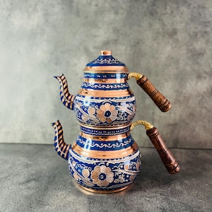 May include: A traditional Turkish tea set with two copper kettles. The kettles are decorated with blue and gold floral patterns. The set has wooden handles.