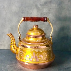May include: A gold and copper teapot with intricate floral designs. The teapot has a wooden handle and a rounded body.