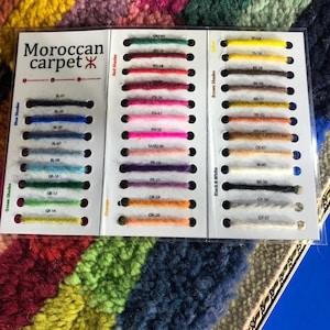 K&ouml;nnte beinhalten: Eine Farbkarte f&uuml;r marokkanische Teppiche mit Garnproben in Blau-, Gr&uuml;n-, Orange-, Rot-, Braun-, Schwarz- und Wei&szlig;t&ouml;nen. Die Karte enth&auml;lt den Text "Moroccan carpet" und Farbcodes f&uuml;r jede Probe.