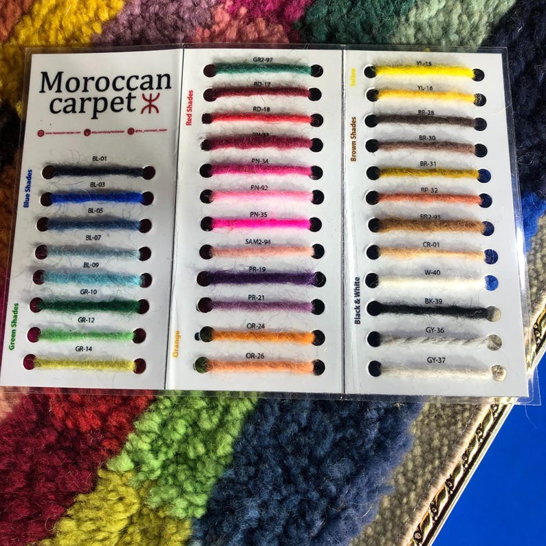 K&ouml;nnte beinhalten: Eine Farbkarte f&uuml;r marokkanische Teppiche mit Garnproben in Blau-, Gr&uuml;n-, Orange-, Rot-, Braun-, Schwarz- und Wei&szlig;t&ouml;nen. Die Karte enth&auml;lt den Text "Moroccan carpet" und Farbcodes f&uuml;r jede Probe.