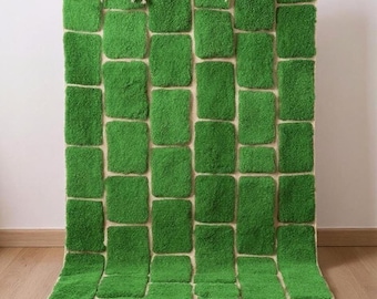May include: A rectangular green rug with a brick-like pattern. The rug features a series of raised, rectangular blocks in a vibrant green color, set against a neutral background. The rug has a fringe along the bottom edge and is approximately 60 inches long.