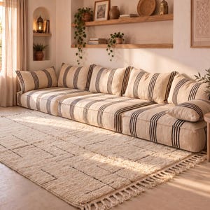 May include: A low-profile modular sofa featuring a cream-colored fabric with vertical black stripes. The sofa consists of multiple connected floor-level seating sections with matching back cushions and a rectangular throw pillow on the right side.