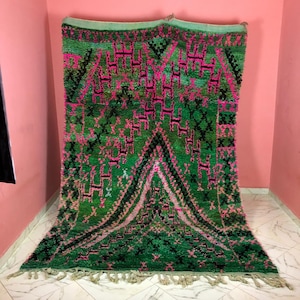 May include: A green and pink Moroccan rug with a geometric pattern. The rug has a fringe border and is made of wool.