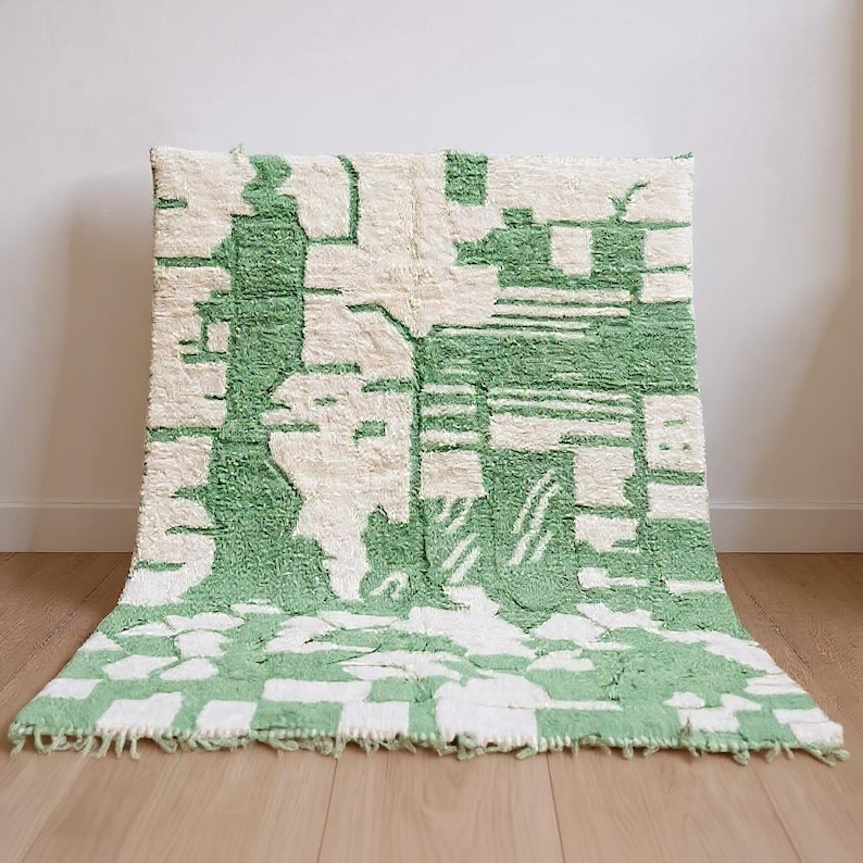 K&ouml;nnte beinhalten: Ein rechteckiger, abstrakter Teppich mit gr&uuml;nem und wei&szlig;em Design. Der Teppich hat ein sich wiederholendes Muster aus geometrischen Formen und Linien in hellgr&uuml;ner Farbe auf wei&szlig;em Hintergrund. Der Teppich besteht aus dickem, strukturiertem Material.
