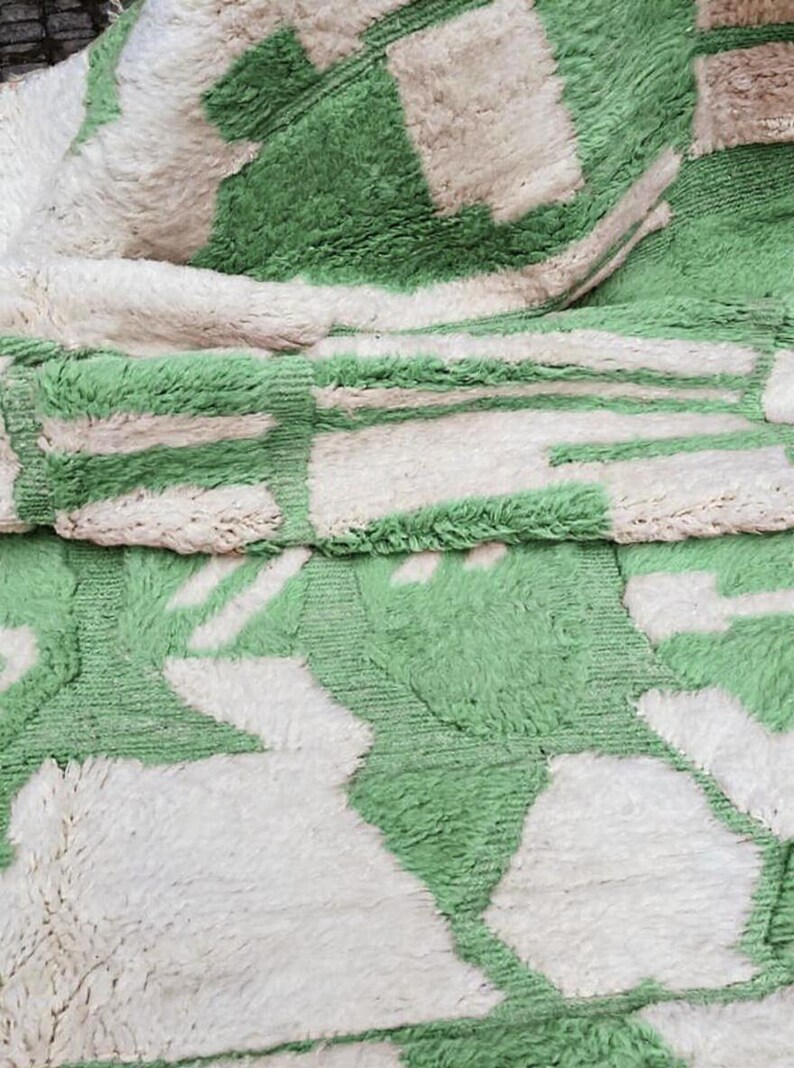 K&ouml;nnte beinhalten: Nahaufnahme eines weichen Teppichs mit einem geometrischen Muster in Gr&uuml;n und Off-White. Das Design zeigt rechteckige und abstrakte Formen, die einen optisch ansprechenden Textil schaffen. Die Textur des Teppichs ist weich.