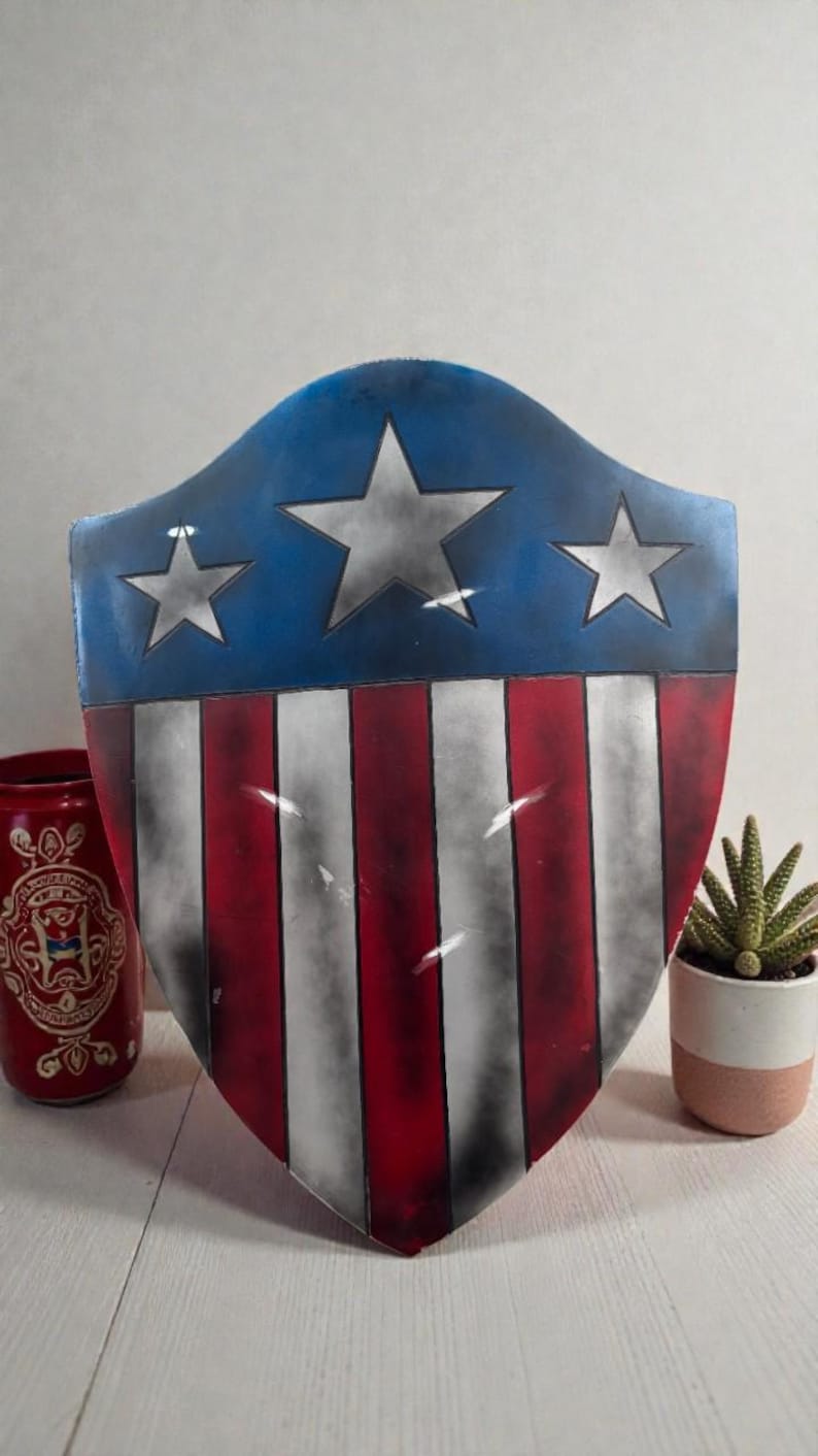 May include: A shield with a blue top section featuring three white stars. The lower section has red and white vertical stripes. The shield is a patriotic design, reminiscent of a superhero's emblem.