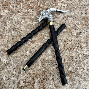 May include: A black walking cane with a silver dragon head handle and a twisted shaft. The dragon head has red accents. The cane has gold-coloured metal accents at the top and bottom of the shaft.