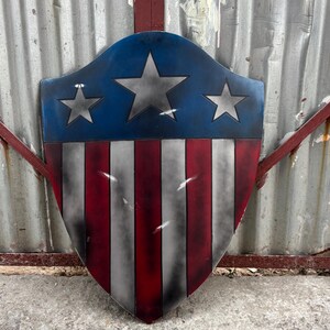 May include: A shield with a blue top section featuring three silver stars, and a red and white striped bottom. The shield is a patriotic design, reminiscent of the American flag.
