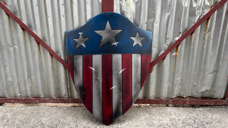 May include: A shield with a blue top section featuring three silver stars, and a red and white striped bottom. The shield is a patriotic design, reminiscent of the American flag.
