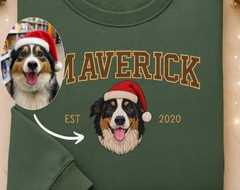 May include: A dark green sweatshirt with the word "MAVERICK" in a tan, collegiate-style font. Below the word is a graphic of a dog wearing a Santa hat. The sweatshirt also has the text "EST 2020".