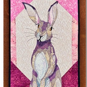 May include: A quilt block featuring a purple and brown rabbit with pink ears, set against a pink and purple background. The block is titled "Twitch" and is part of a series called "Hare They Are!" The block measures 12 1/2 inches by 20 1/4 inches.