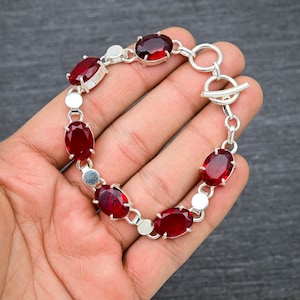 Peut inclure: Un bracelet en argent avec un fermoir à glissière présente six pierres précieuses rouges de forme ovale.
