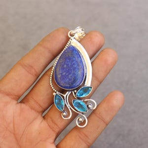 Peut inclure: Un pendentif en argent orné d'une grande pierre de lapis-lazuli bleu profond en forme de poire avec des éclats dorés, accentué par trois petites pierres de topaze bleu clair taille marquise sur une monture en métal décorative avec bélière.