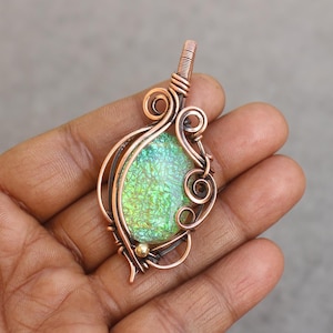 May include: A handcrafted copper pendant with a vibrant green and gold iridescent glass stone. The pendant features intricate wire wrapping with decorative swirls and a small gold bead accent. The overall design is organic and artistic.