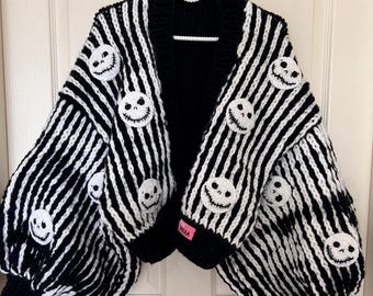 May include: A black and white striped cardigan with white skull appliqués. The long-sleeved sweater has a black collar and cuffs. The sleeves are puffy. The cardigan is hanging on a white hanger.