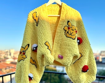 May include: A yellow, chunky-knit cardigan with Pikachu and lightning bolt appliques. The long-sleeved sweater also features red and white Pokeball accents. The cardigan is hanging on a white hanger against a blue sky.