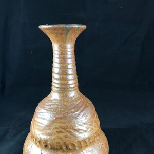 May include: A brown ceramic vase with a textured surface and a wide, round base. The vase has a narrow neck and a flared opening.