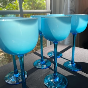May include: A set of five stemmed glasses featuring opaque, light blue bowls that transition into deep, translucent blue stems and circular bases. The glasses have a smooth, rounded silhouette with a consistent color gradient from top to bottom.