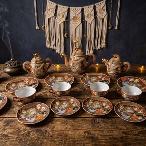 May include: A tea set featuring a teapot, two lidded sugar bowls, and multiple saucers and cups decorated with intricate dragon motifs and religious figures. The ceramic pieces are brown with gold accents and white interiors.