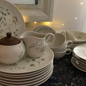 May include: A set of white ceramic dishes with a floral pattern. The set includes a sugar bowl with a wooden lid, a creamer, cups, saucers, and plates.