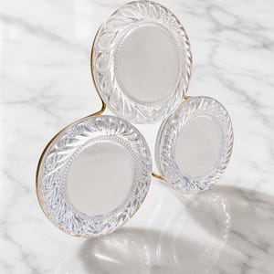 May include: A triple-frame mirror featuring three circular glass panels with ornate, molded leaf-like patterns along the edges. The frames are connected by a thin, gold-toned metal structure that supports the arrangement in a triangular formation.