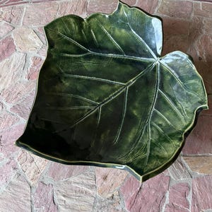 May include: A large, dark green ceramic leaf-shaped serving dish. The dish has detailed veining and a glossy finish. The leaf design is a unique decorative piece, perfect for serving food or as a decorative accent.