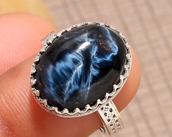 Puede incluir: Anillo de plata ovalado con una piedra preciosa azul pulida. La piedra tiene un patrón arremolinado y está engastada en un bisel de plata decorativo. La banda del anillo presenta un diseño detallado.