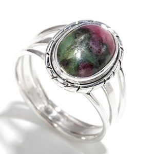 May include: A sterling silver ring featuring an oval-shaped gemstone with a mix of red and green hues. The ring has a split shank design with three parallel bands on each side of the gemstone setting. The gemstone is approximately 0.75 inches long.