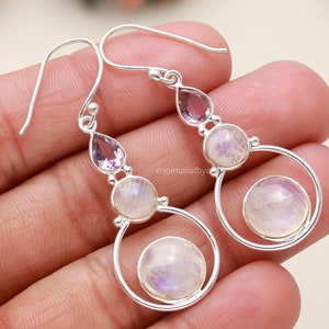 Puede incluir: Pendientes de plata con un diseño de piedra lunar y amatista. Los pendientes tienen un diseño circular con una piedra lunar más grande en el centro.