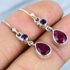 Puede incluir: Pendientes de plata con una piedra preciosa de rubí en forma de lágrima y una pequeña piedra preciosa redonda de amatista.