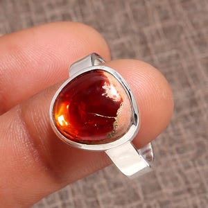 Puede incluir: Anillo de plata con una gran piedra preciosa en forma de lágrima, de color marrón rojizo intenso. La piedra está engastada en una banda de plata pulida. El diseño del anillo es sencillo y elegante, adecuado para cualquier ocasión.