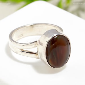Puede incluir: Un anillo de plata con una piedra preciosa de ágata marrón y verde. El anillo tiene un diseño de banda dividida.