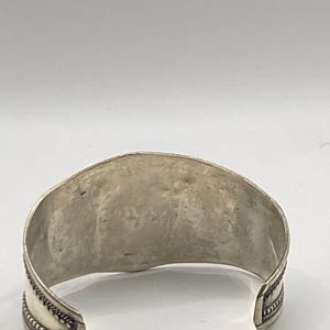 May include: Silver cuff bracelet with a textured design and a decorative border.