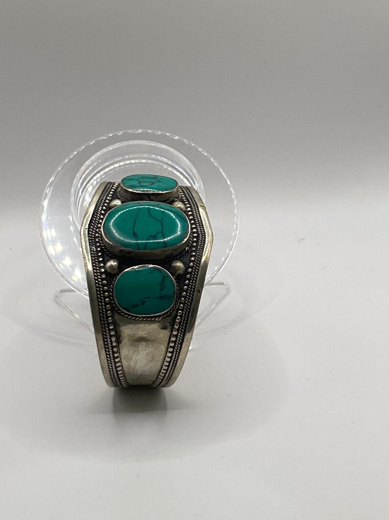 May include: Silver bracelet with three turquoise stones set in a decorative design.